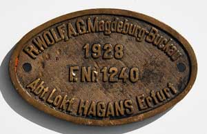 Fabrikschild R. Wolf AG, Magdeburg-Buckau, Abt. Lokfabrik Hagans Erfurt. Fabriknummer: 1240, Baujahr: 1928. Messingguss oval, Riffelgrund mit Rand. BxH = x mm. Das schöne Fabrikschild ist von der DRG/DB 64 084.